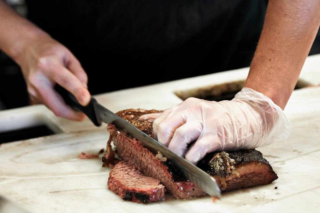 Hands are shown cutting a smoked slab of brisket on a cutting board